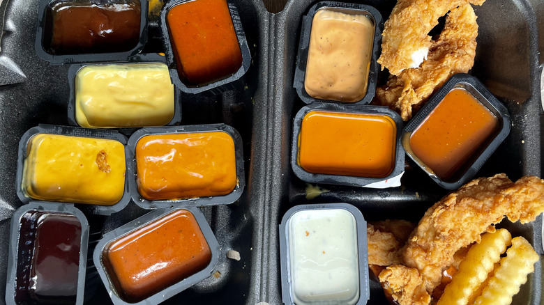Assorted open sauces, fries, and chicken fingers in a black box