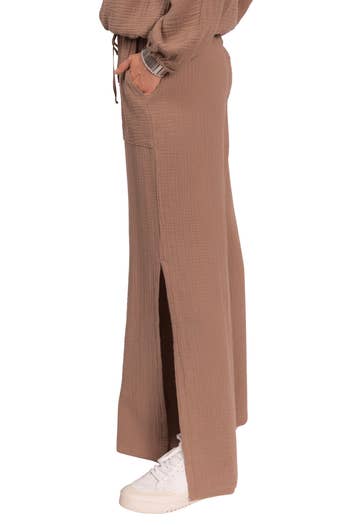 Person wearing wide-leg, ankle-length pants with side pockets and white sneakers. Pants have subtle texture and split hem detail