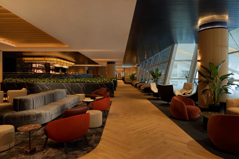 A seating area and angled windows in the foreground with a bar area in the background at the Chase Sapphire Lounge at DFW airport