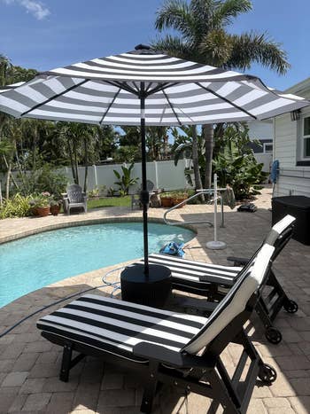 Two striped lounge chairs and an umbrella by a pool, surrounded by potted plants and a tropical setting. Ideal setting for outdoor relaxation