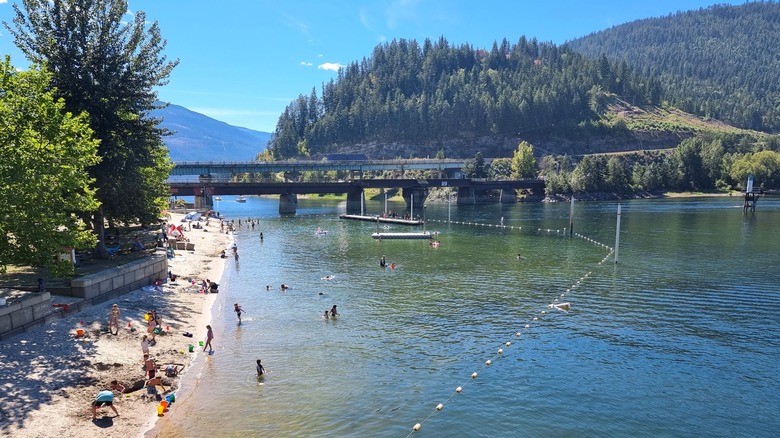 Families playing in the water at Sicamous Beach Park with two low bridges crossing a narrow part of the tree-lined lake