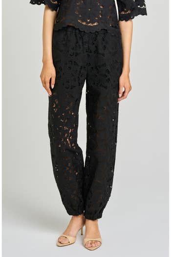 Person wearing stylish crochet lace pants with scalloped edges, paired with a matching top, and **** heels