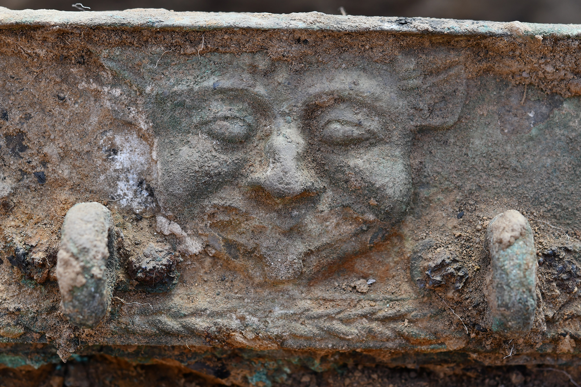 A close up of a bronze chariot with a face carved into it.