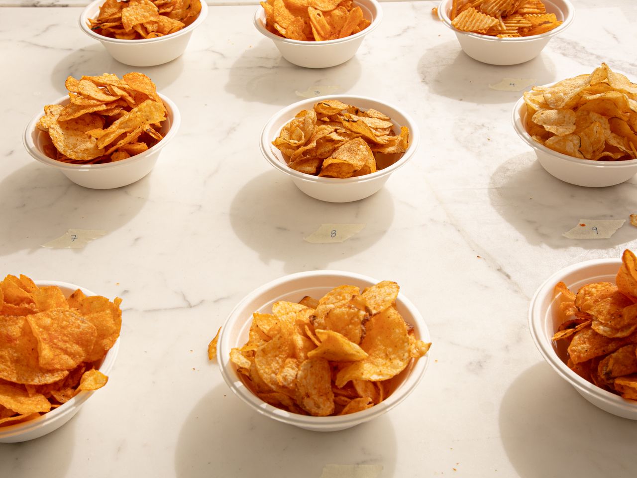 White bowls filled with assorted potato chips arranged on a marble surface