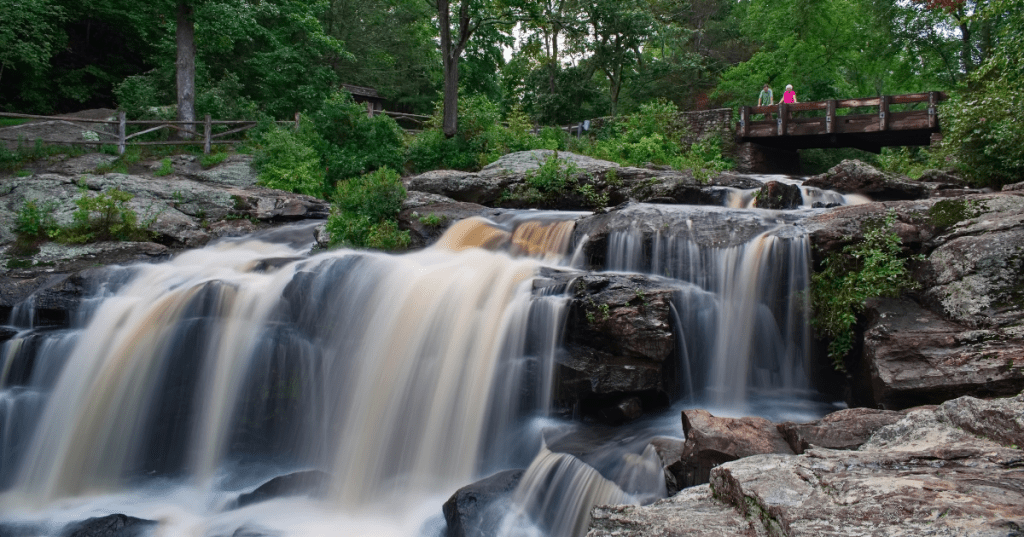 visitors at a bridge look out at a waterfall in Devil's Hopyard State Park, East Haddam, CT