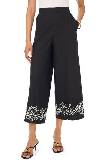 Woman wearing wide-leg pants with floral embroidery at the hem, paired with heeled sandals