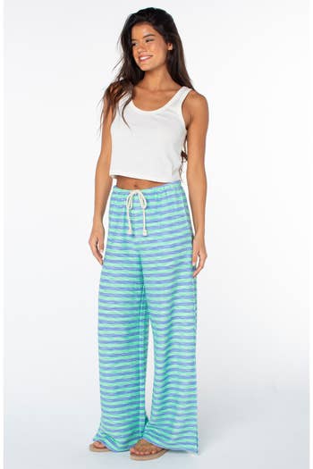 Woman wearing a sleeveless top and loose-fitting striped pants, smiling casually
