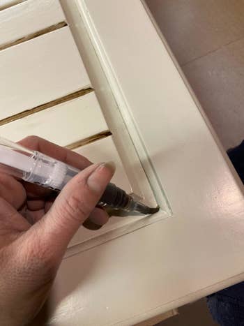 Hand using a paintbrush pen to clean or detail the corner of a slatted white surface