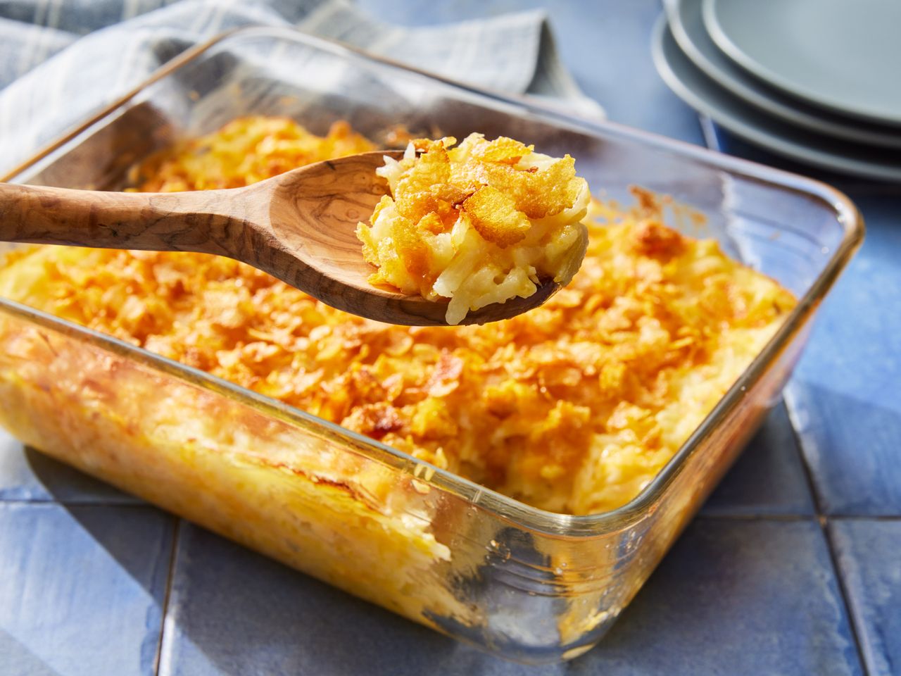 A baking dish of Simply Potatoes cheesy hash browns, with a wooden spoon removing a scoop