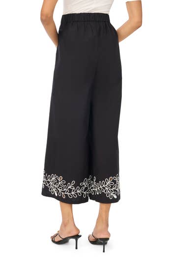 Woman wearing black wide-leg pants with white embroidered leaf pattern at the hem, paired with black heels
