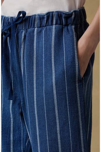 Close-up of a person wearing striped, relaxed-fit pants with an elastic waistband and a drawstring, showcasing casual, comfortable style