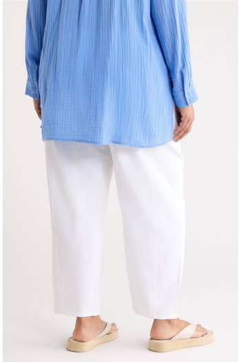 Person wearing a blue long-sleeve shirt, white pants, and sandals, seen from the back
