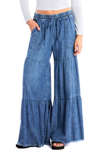 Wide-leg denim pants with tiered ruffle design, worn with a white long-sleeve top
