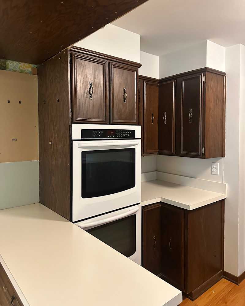 Kitchen corner with dark wood cabinets, white oven, and light countertops.