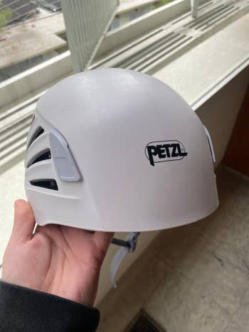 Person holding a white Petzl climbing helmet indoors near a window