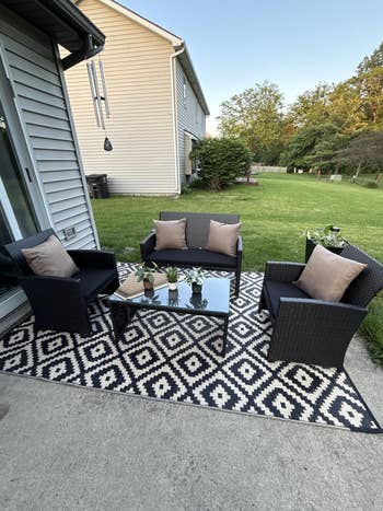 Patio set on a geometric rug with two chairs, loveseat, and glass table; small potted plants as decorations