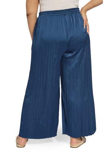 Person wearing wide-leg, pleated pants with a high elastic waistband, shown from the back