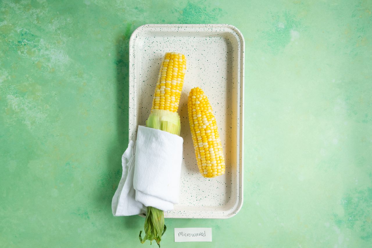 Cooked ears of corn on a serving tray one wrapped partially in a cloth