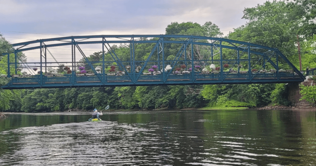 a kayaker goes under the drake hill flower bridge in simsbury ct