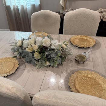 Elegant dining table with neutral decor features a floral centerpiece and gold textured placemats, set for a stylish and modern home setting