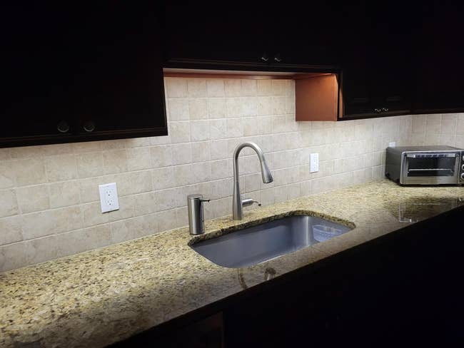 Modern kitchen counter with granite surface, under-cabinet lighting, stainless steel sink, and a small toaster oven