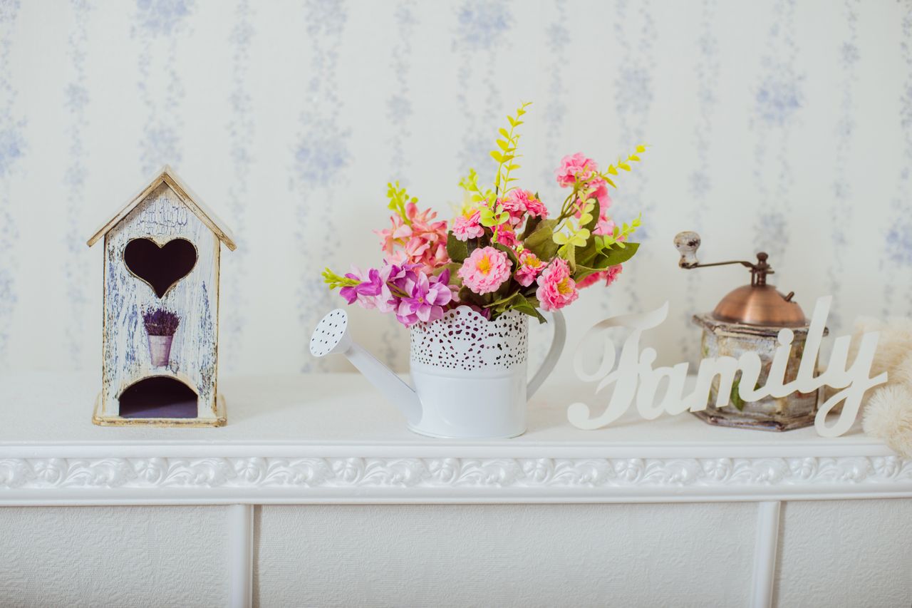 A decorative setup featuring a birdhouse a watering can vase with flowers and a Family sign on a shelf