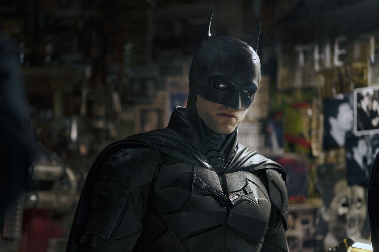 A person in a batthemed costume standing in a dimlylit room with various items on the walls