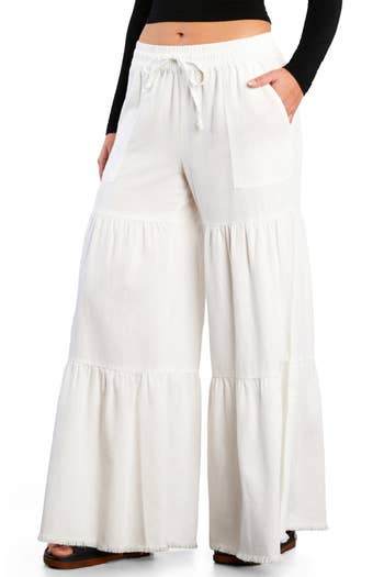 Woman wearing wide-leg tiered pants with drawstring waist, hands in pockets, styled casually