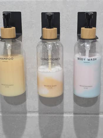Three labeled pump bottles on a wall: shampoo, conditioner, body wash. Each bottle reads