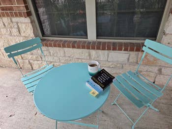 Outdoor scene with two chairs and a table holding a coffee mug and a book titled