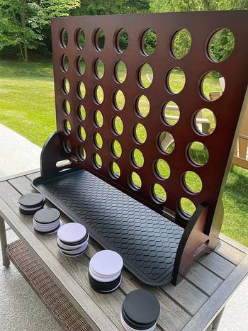 Giant wooden Connect Four game on a table outdoors, with black and white discs placed in rows at the bottom
