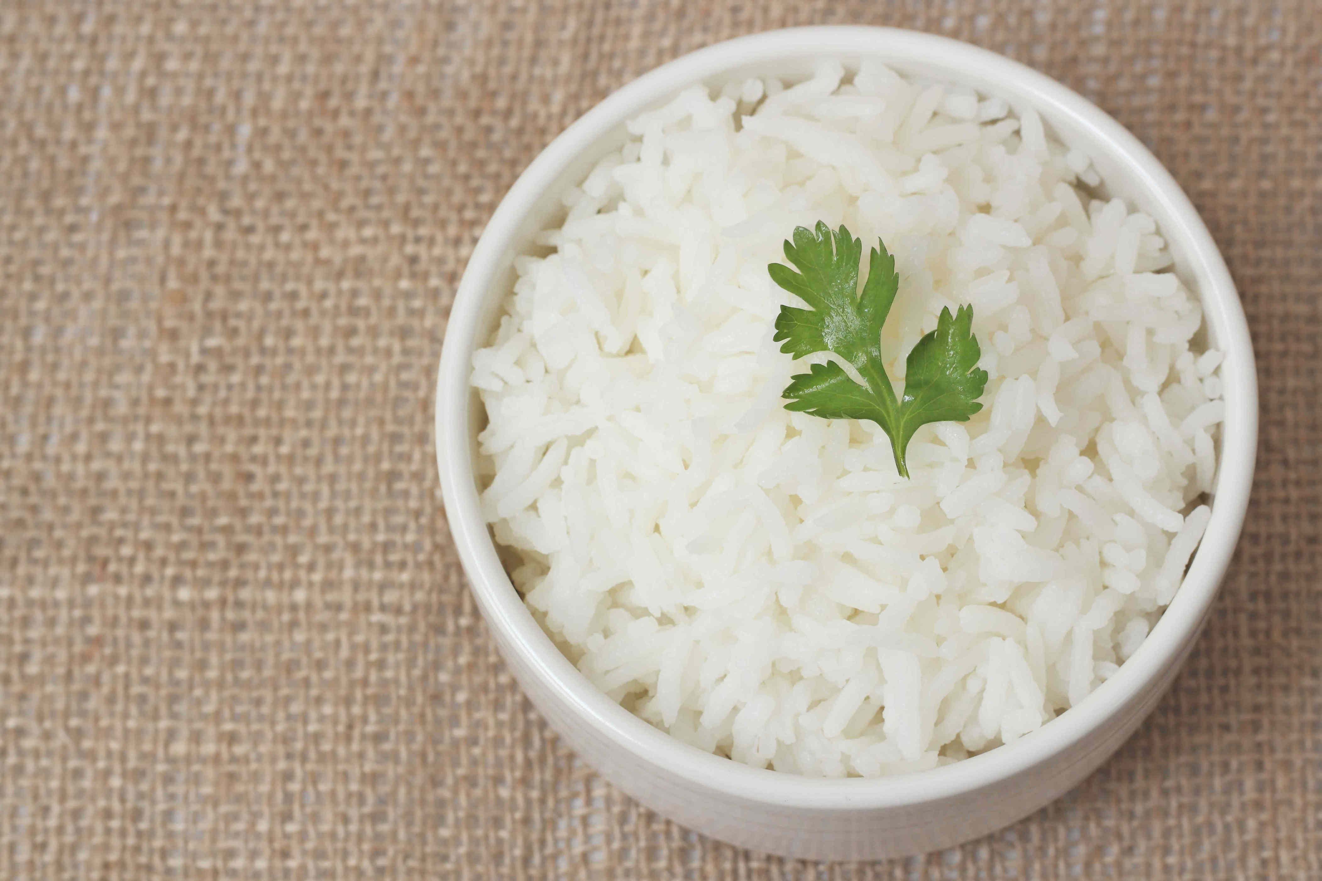 A bowl of rice garnished with a sprig of parsley on a burlap background