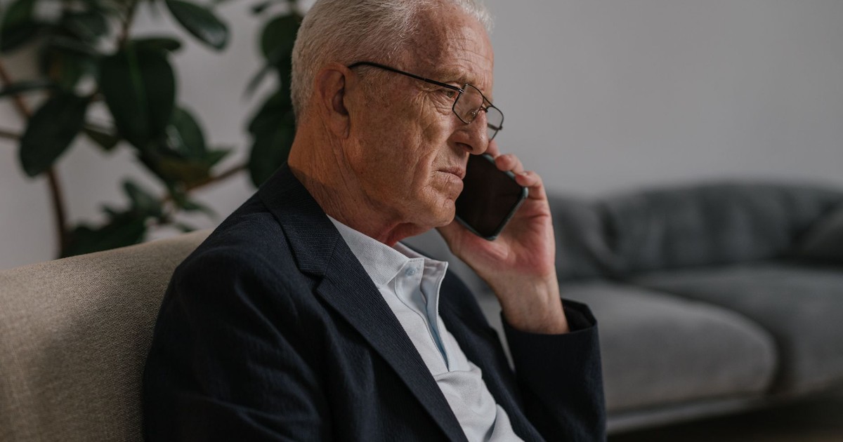 Senior man with eyeglasses sitting indoors, having a phone call. Calm and thoughtful atmosphere.
