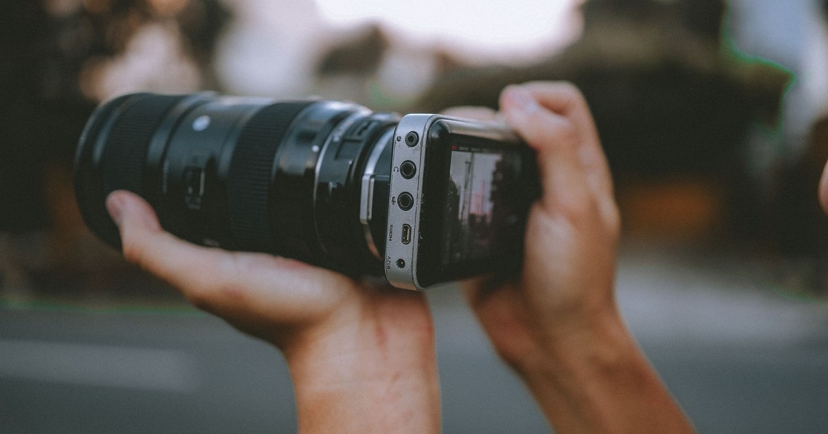 Hands holding a smartphone camera adapter with lens outdoors.