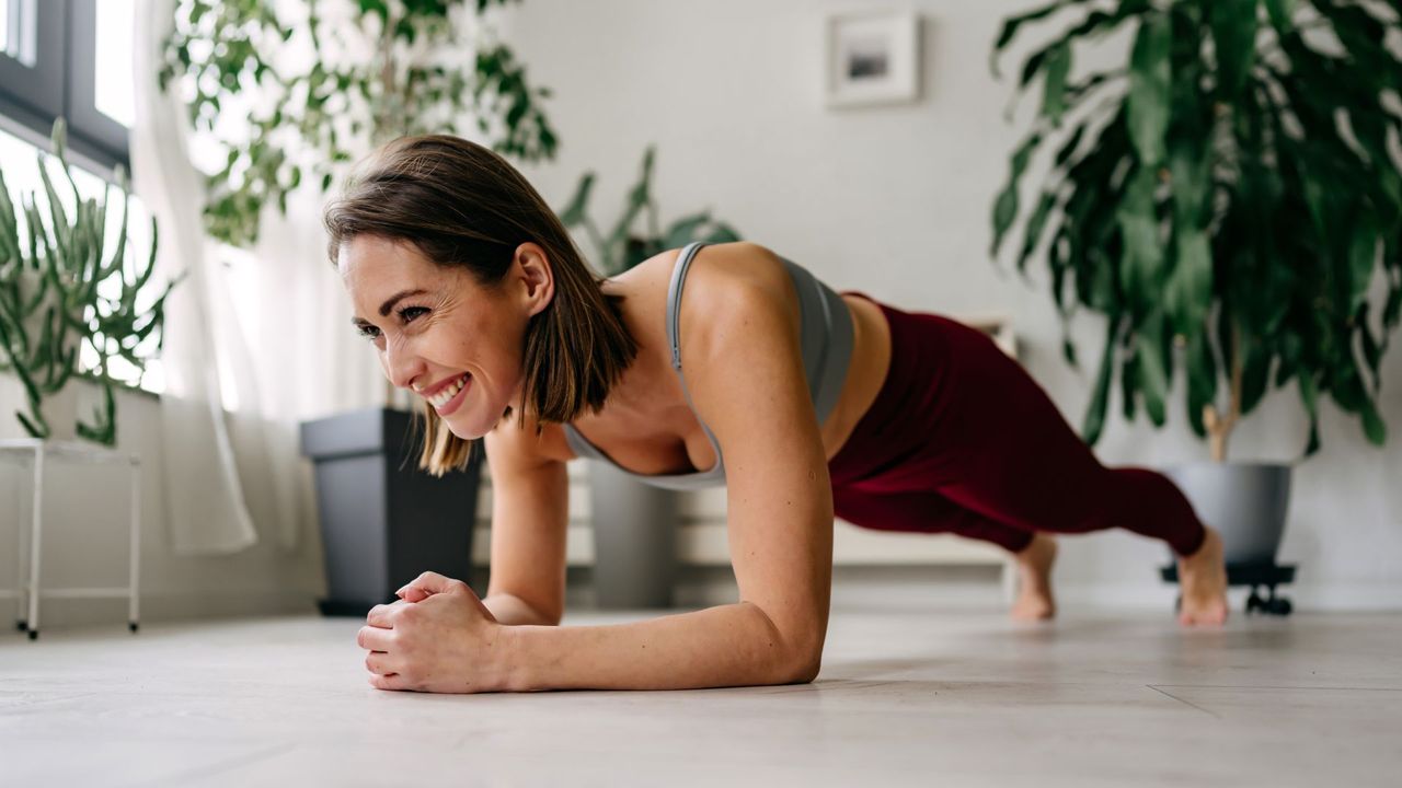 Woman setting up for plank rows exercise at home, smiling on floor