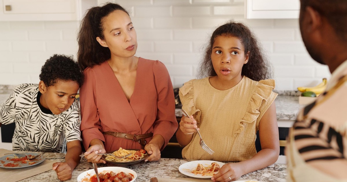 A family gathers around the kitchen table enjoying a pasta meal together.