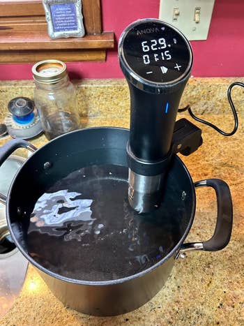 Sous vide immersion circulator in a pot with water at 62.9°C, timer showing 1:15. Kitchen counter setting