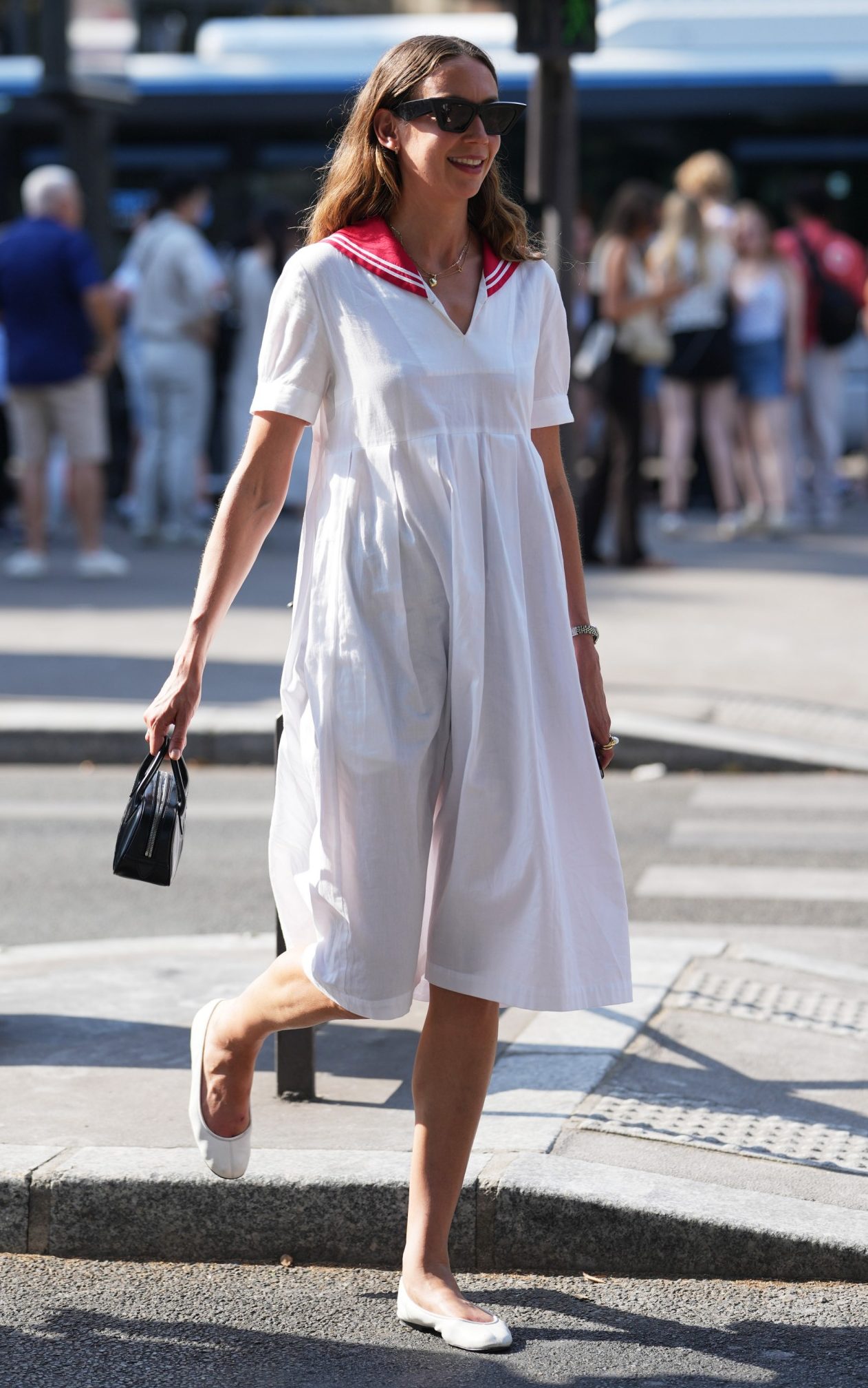 A guest wears medium-length wavy brown hair, black squared sunglasses, a white midi dress with a red sailor collar, and white leather ballet flats shoes, outside Comme des Garçons during Paris Fashion Week in June 2026
