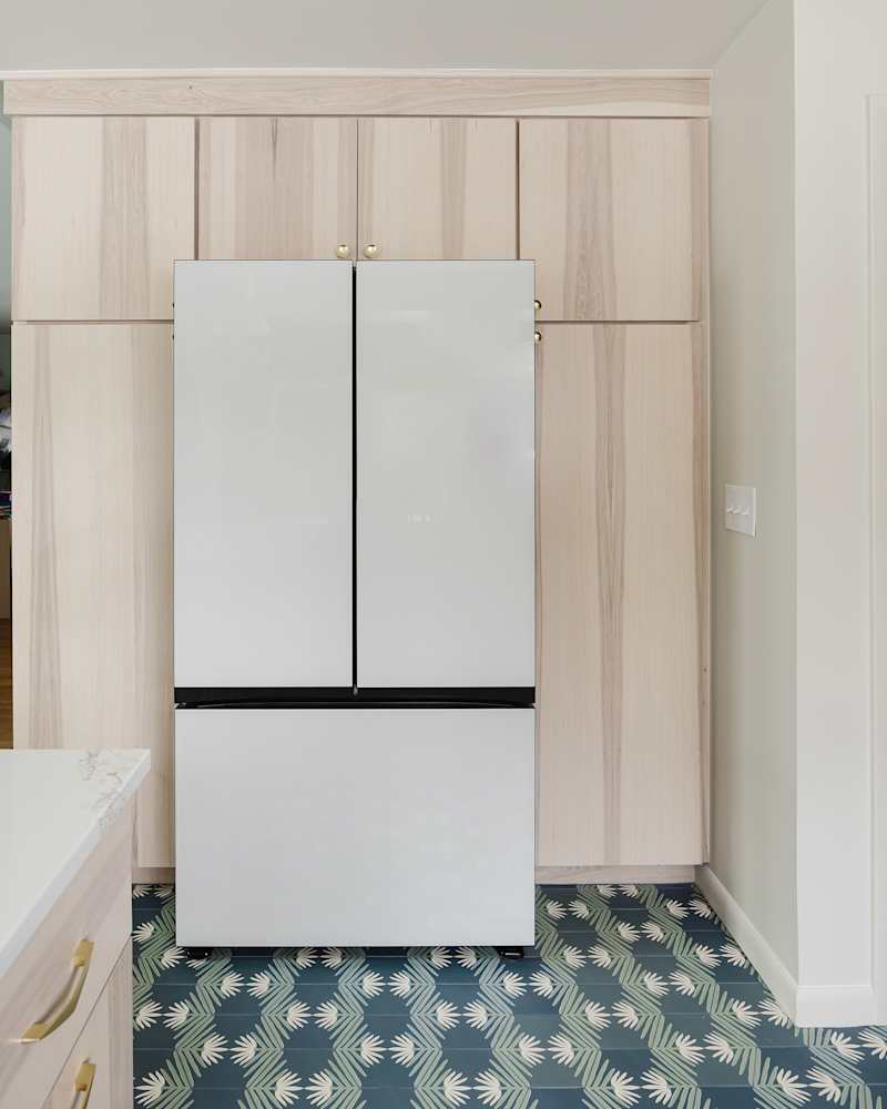Modern kitchen featuring a white refrigerator with black accents, light wood cabinetry, and a patterned green and white floor.