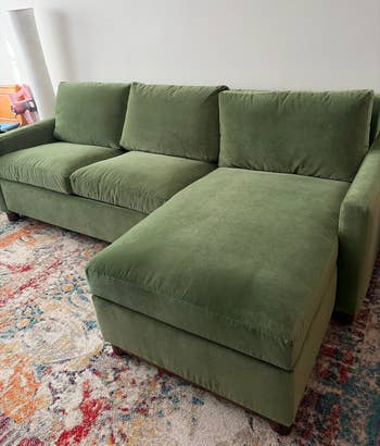 Green upholstered sectional sofa with a chaise, set in a cozy, brightly patterned room