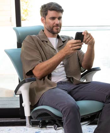 Model seated comfortably in ergonomic chair, using smartphone