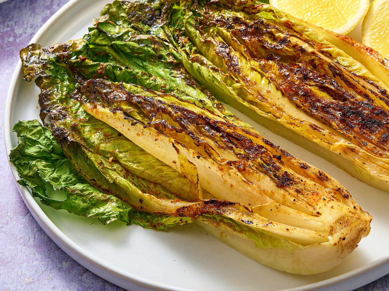 Grilled romaine lettuce served on a plate alongside lemon wedges