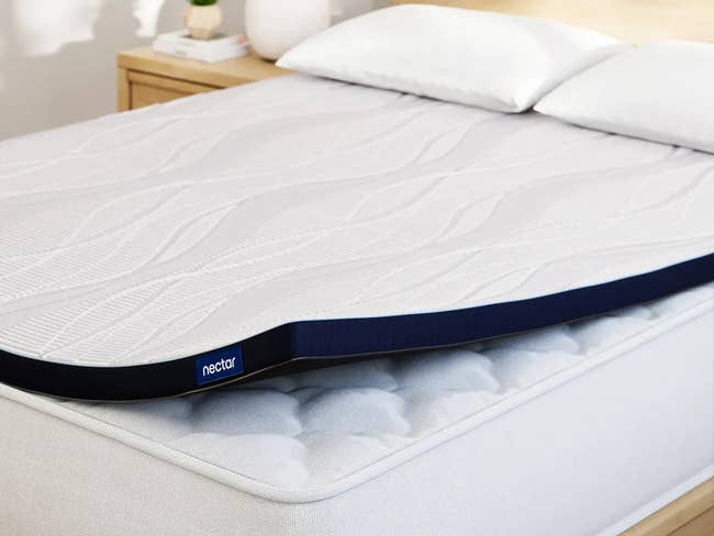 A memory foam mattress topper on a bed with pillows, featuring a wavy pattern and a branded edge