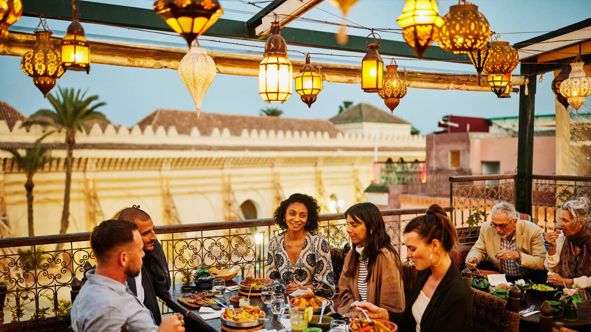 wide-shot-of-tourists-laughing-and-savoring-traditional-moroccan-tajine-at-scenic-rooftop-eatery-during-holiday-in-marrakech-at-night-stockpack-gettyimages