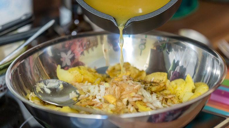Someone pouring bacon grease into a metal bowl to make German potato salad