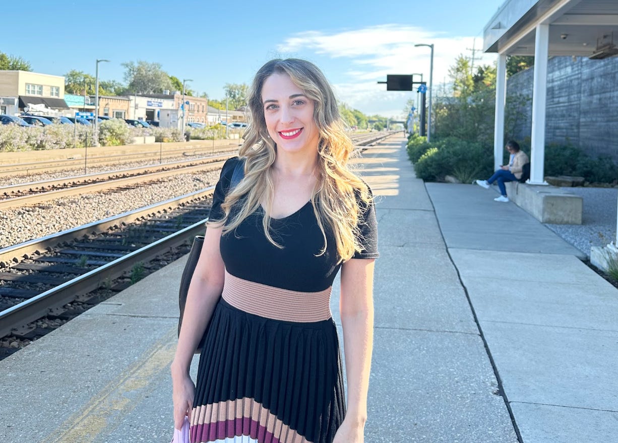 The writer wearing a dress and standing in front of a train station in Illinois.