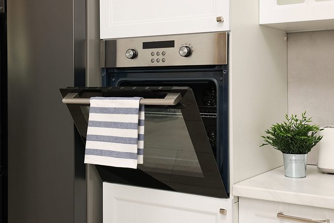 Open Electric Oven With Striped Towel In Kitchen. Cooking Appliance