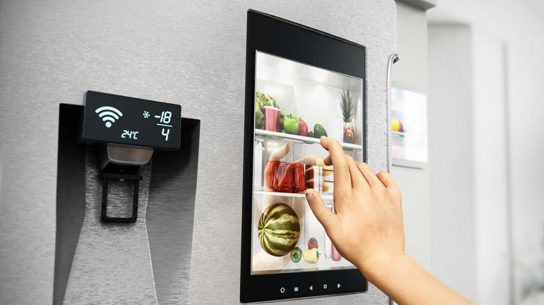 A hand touching a screen on a smart fridge.
