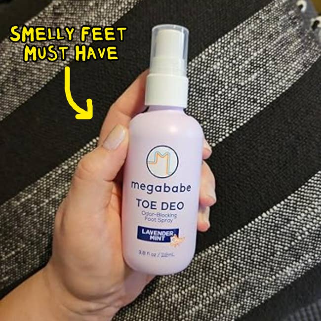 Hand holding Megababe Toe Deo foot spray with lavender scent, captioned