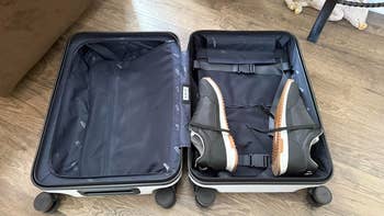 Open suitcase on wheels with a pair of black sneakers neatly strapped inside on a wooden floor